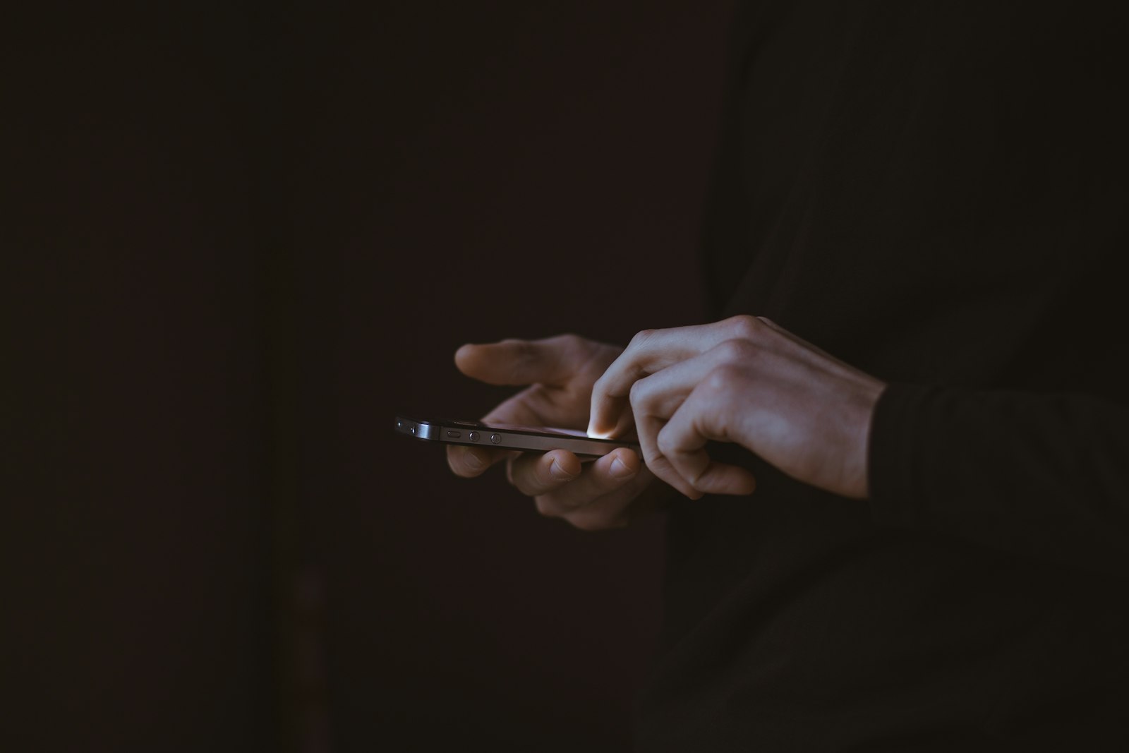 Hands typing on a smartphone in the dark